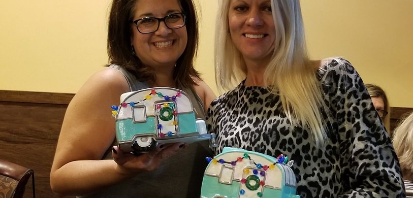Two women showing off their painted ceramic campers